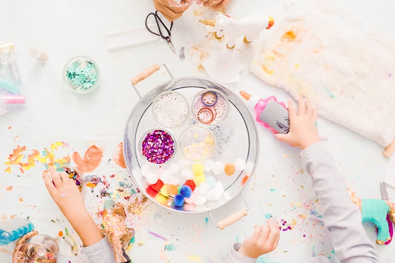 image of children's hands at a messy covered table with art decorations