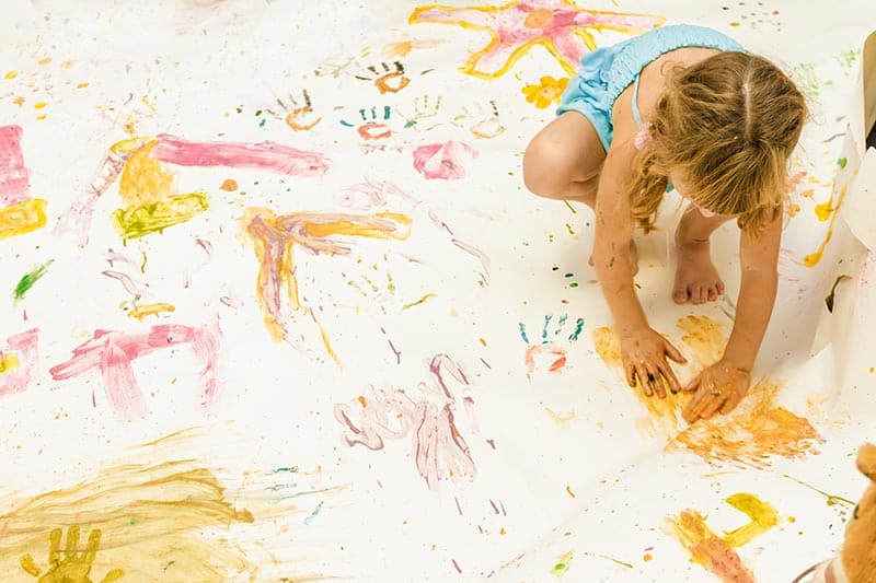 image of a young girl painting with her hands on paper set out on the floor