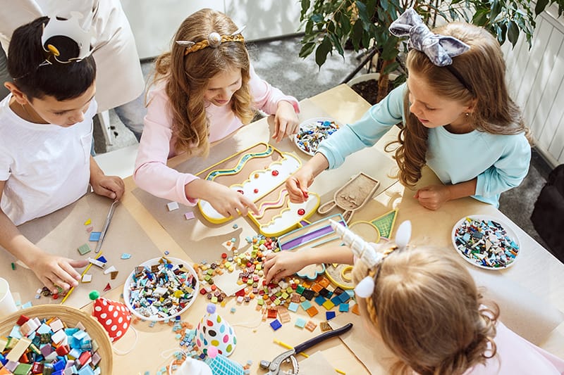 image of children and birthday decorations. One little boy and three little girls are at a table with edible food decorations as art supplies.