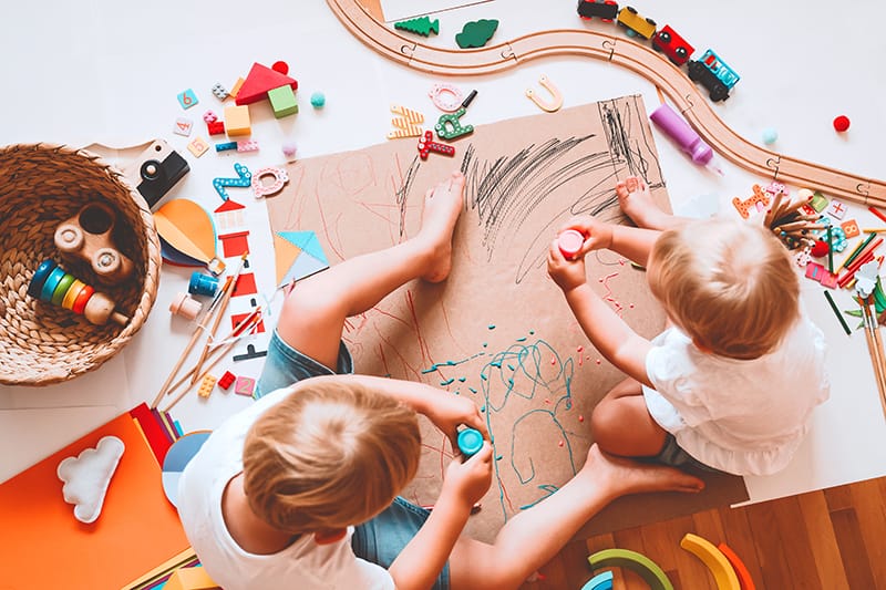 image of two kids pouring paint out of a bottle onto construction paper. They are surrounded by toys.